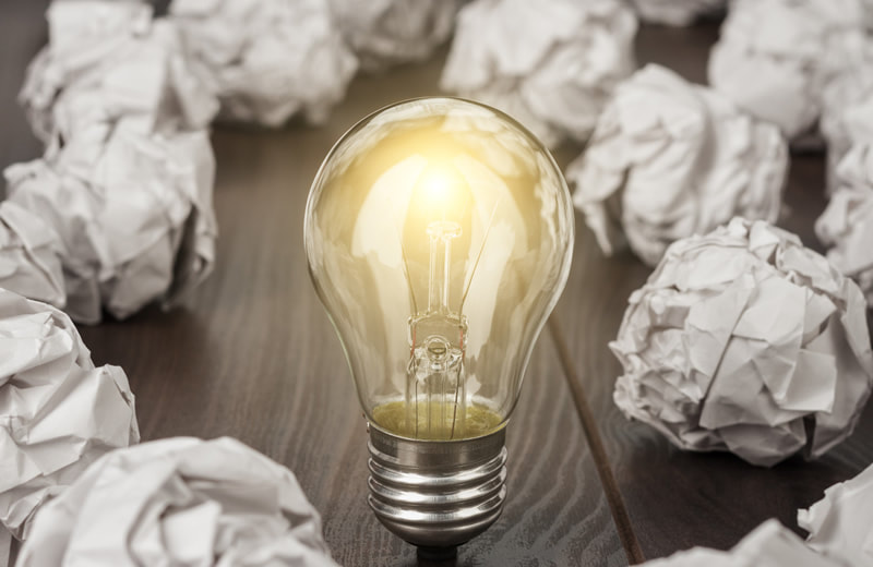 Light bulb standing on table surrounded by crumpled pieces of paper