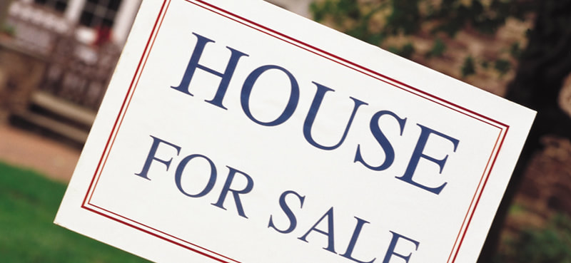 House for Sale yard sign with home blurred in the background