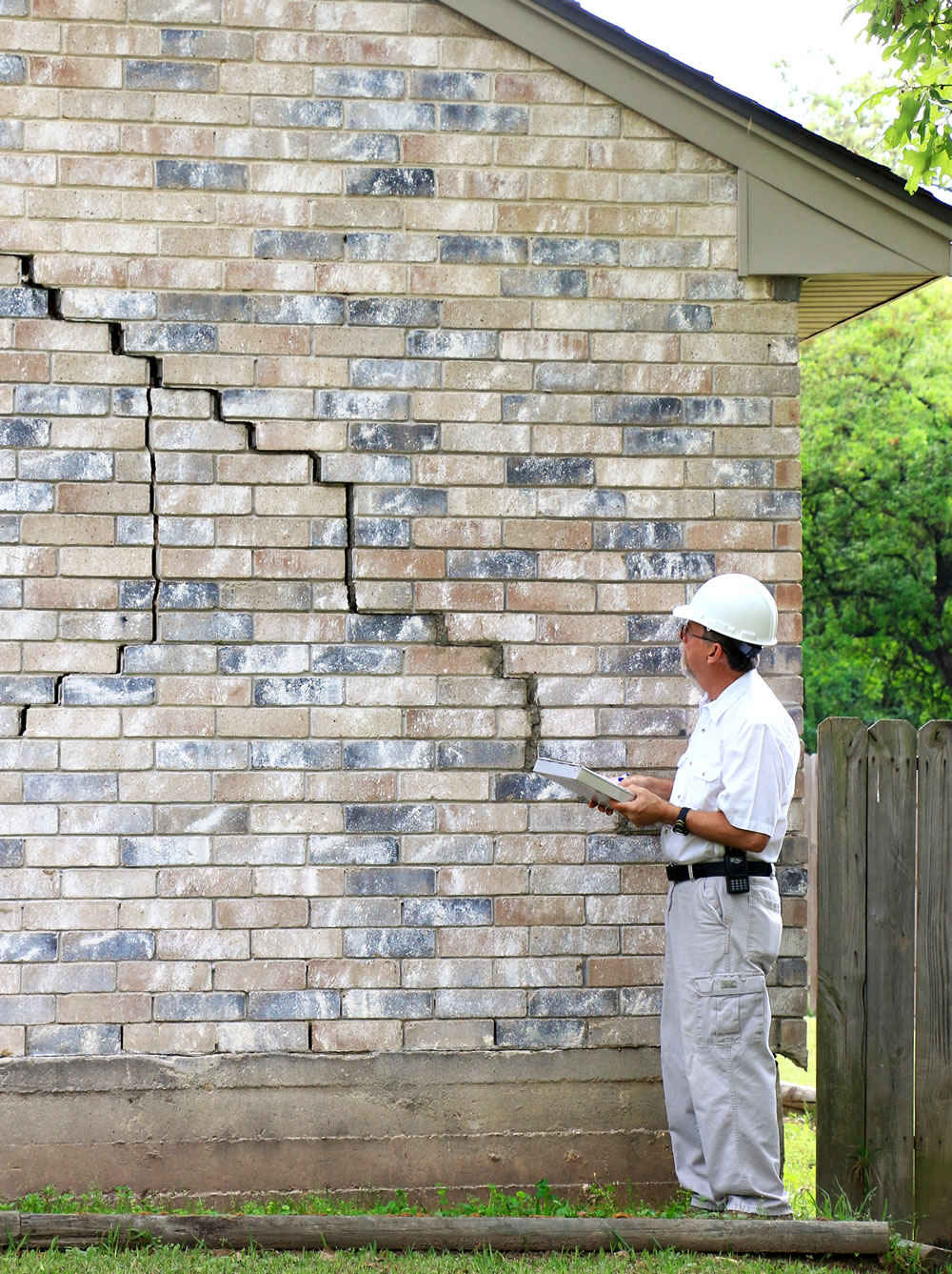 Inspector standing next to brick home with diagonal crack in brick